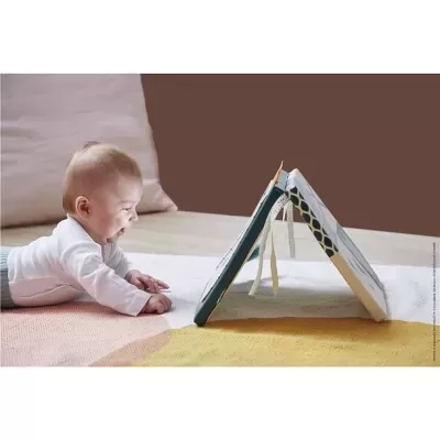 Bebé deitado a olhar para um livro ambiental em formato de tenda numa superfície almofadada multicolor