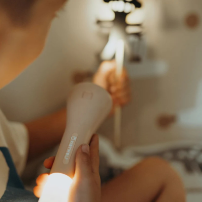 Dispositivo elétrico portátil branco com texto 'TRIMMER' nas mãos de criança em ambiente interno