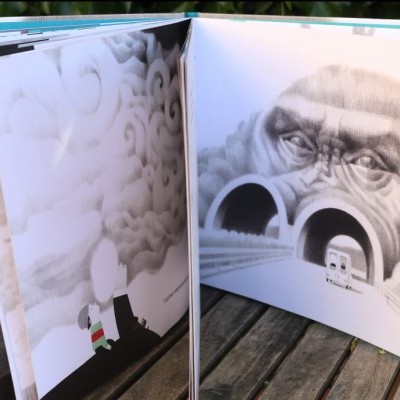 Livro aberto com ilustrações em preto e branco, incluindo um gorila e uma chaminé, sobre mesa de madeira ao ar livre