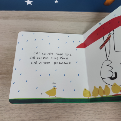 Livro infantil aberto com texto e ilustrações de pintainhos e gotas de chuva.