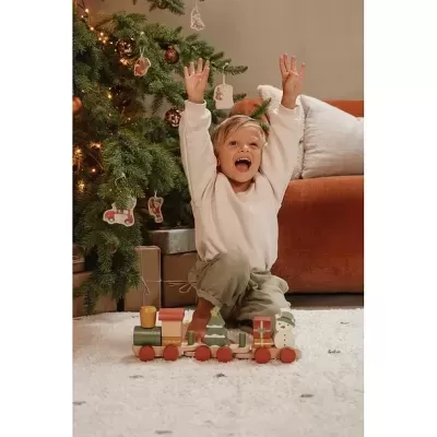 Brinquedo de comboio de madeira colorida ao lado de árvore de Natal decorada, com criança e sofá ao fundo