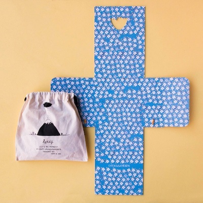 Embalagem azul floral desdobrada e saco de tecido bege com ilustração de urso e texto