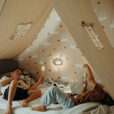 Tenda infantil de tecido bege sobre cama com crianças e decoração de parede com nuvens e pontos