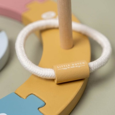 Brinquedo infantil colorido com anel de tecido branco e peça em madeira amarela com texto LITTLE DUTCH