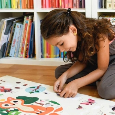 Criança a montar puzzle colorido no chão em frente a estante de livros