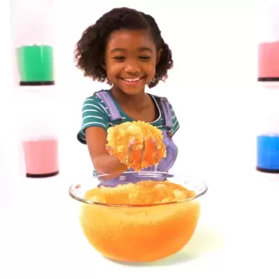 Menina segurando slime laranja numa tigela de vidro