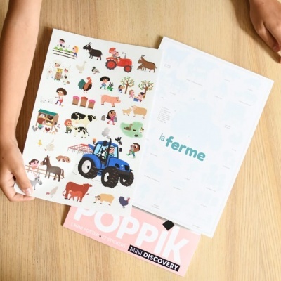 Folhas ilustradas com animais de quinta e tractor azul, texto 'la ferme', revista rosa 'POPPIK MINI DISCOVERY' em mesa de madeira