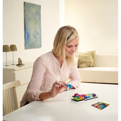 Mulher loira a jogar jogo de tabuleiro colorido numa mesa branca em sala clara