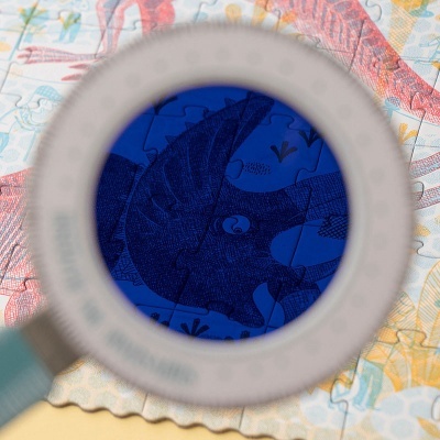 Lupa a ampliar uma zona de puzzle azul com desenho de dinossauro tricerátopo