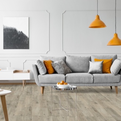 Modern living room with grey sofa, orange cushions and lamps, light wood flooring, and white furniture