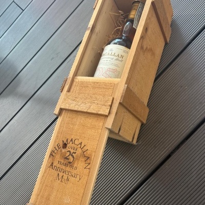 Garrafa de whisky The Macallan Anniversary Malt com mais de 25 anos em caixa de madeira aberta sobre piso cinza