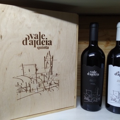 Garrafa de vinho Vale d'aldeia com rótulos branco e preto junto a caixa de madeira gravada