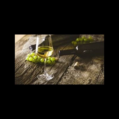 Taça de vinho branco com uvas verdes e garrafa de vinho sobre mesa de madeira rústica