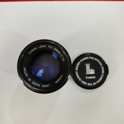 Objetiva Canon Lens FD 50mm 1:1.4 preta com tampa preta com texto de apoio oficial dos Jogos Olímpicos de 1980.