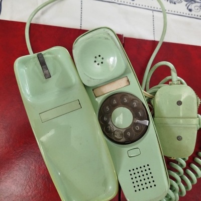 Telefone fixo antigo verde claro com disco rotativo sobre mesa com toalha colorida.