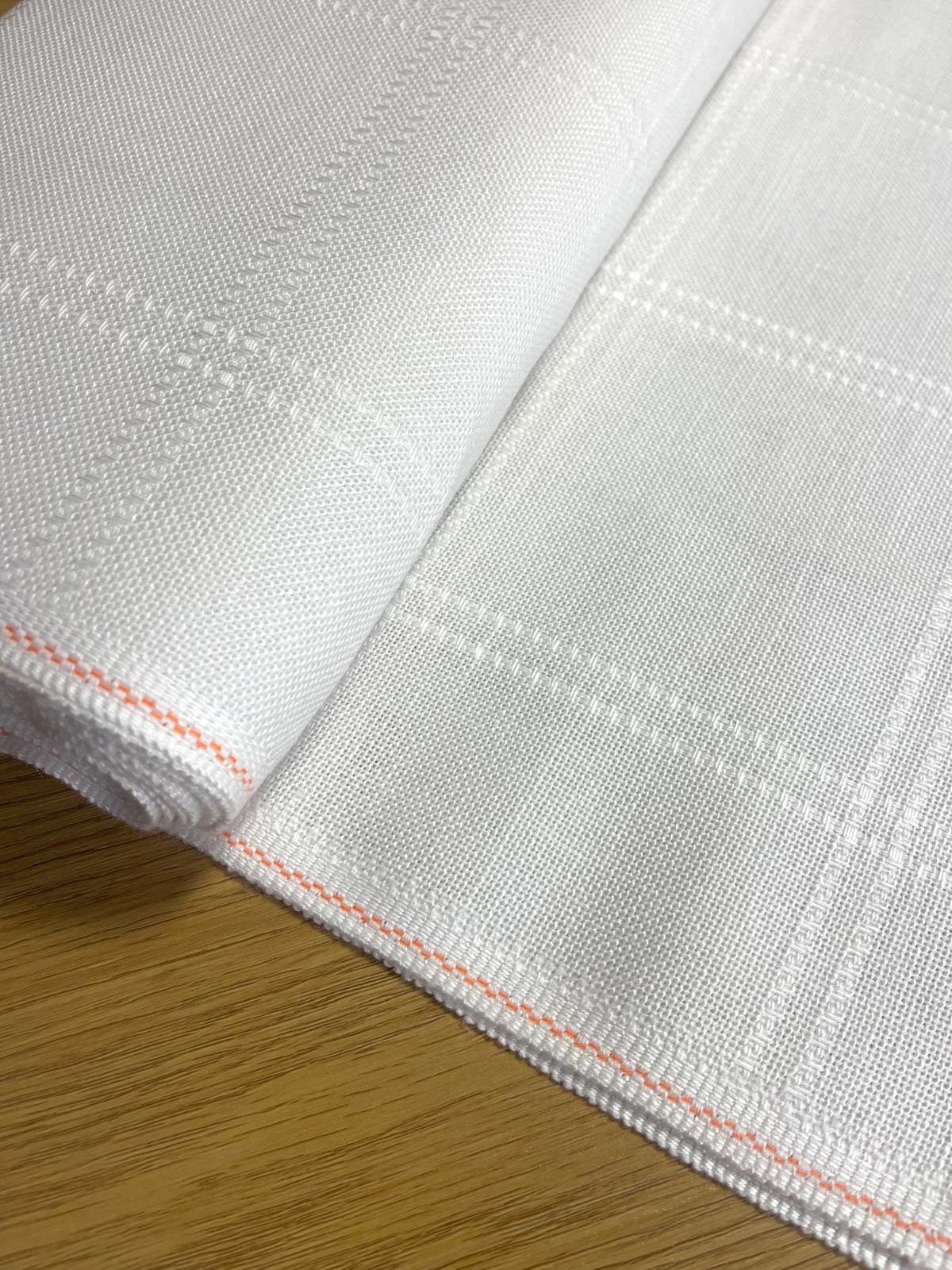 Pano branco com padrão quadriculado e borda laranja sobre mesa de madeira
