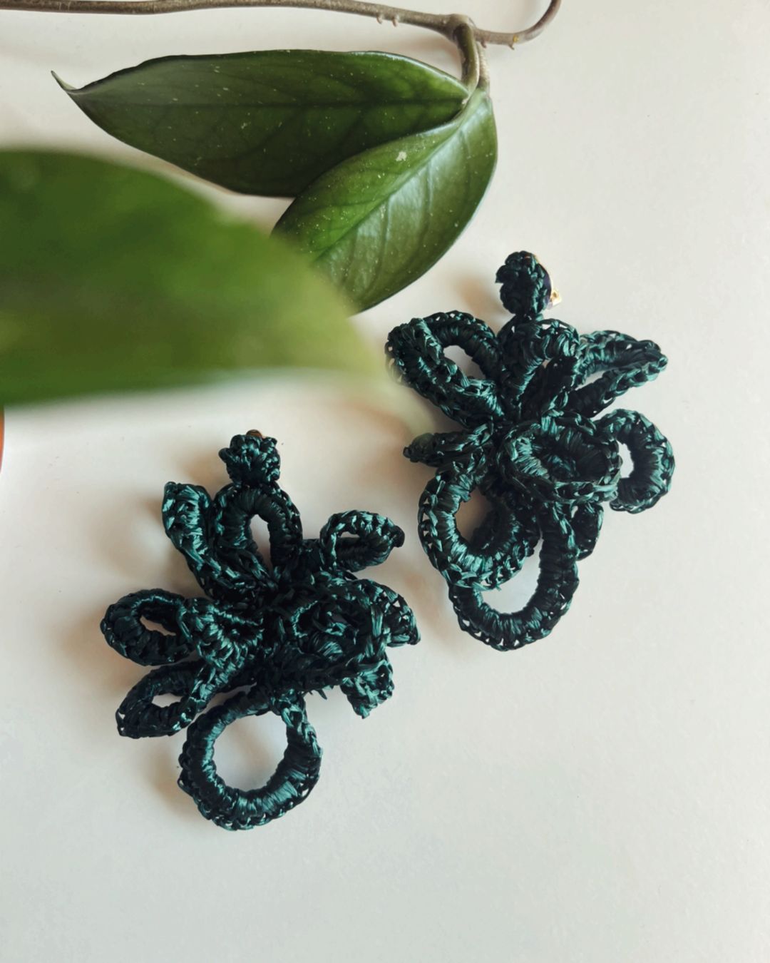 Brincos florais em fio trançado verde escuro sobre fundo branco com folhas verdes