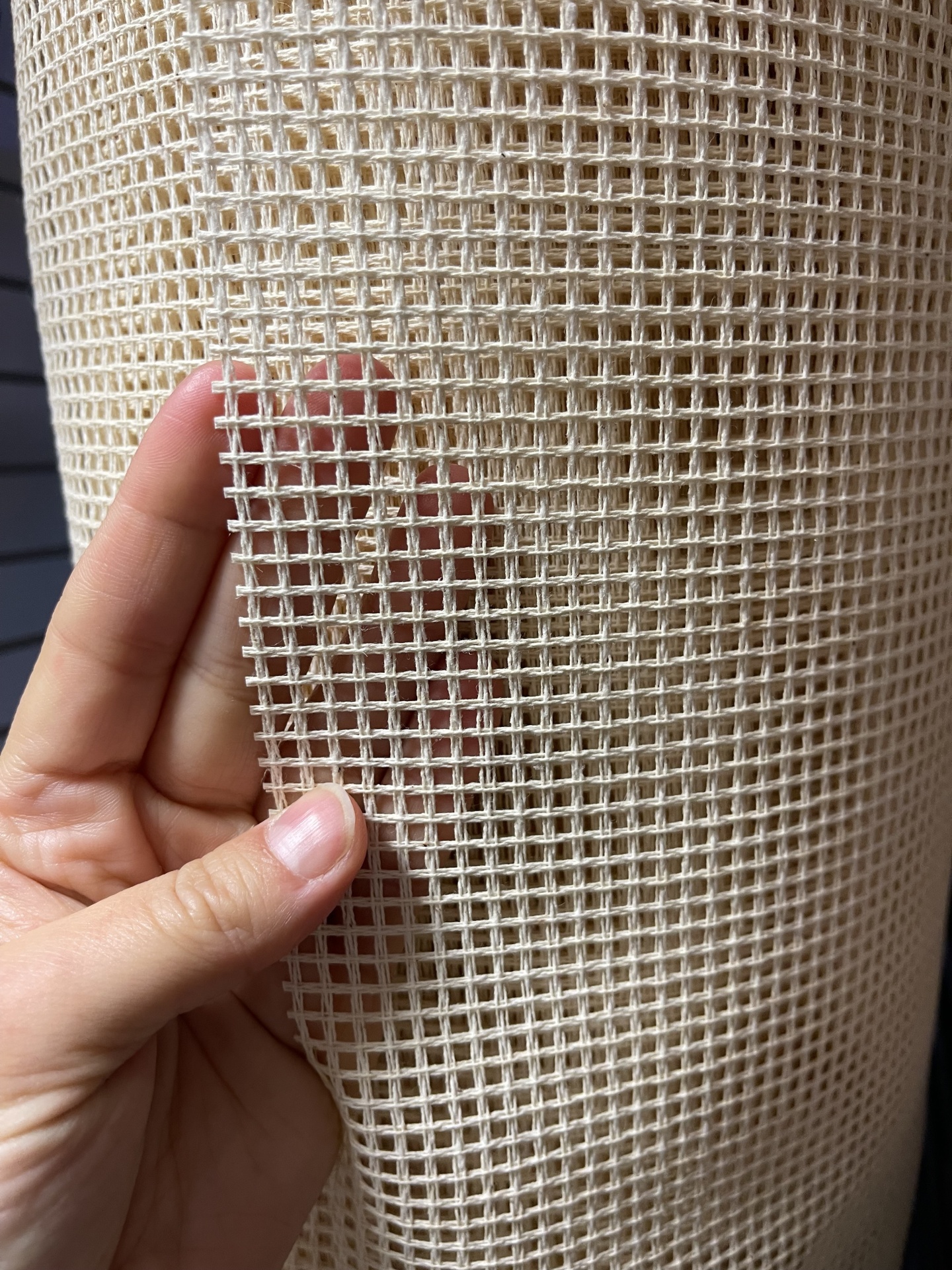 Tecido de algodão cru com padrão de malha quadrada aberta com mão a segurá-lo.