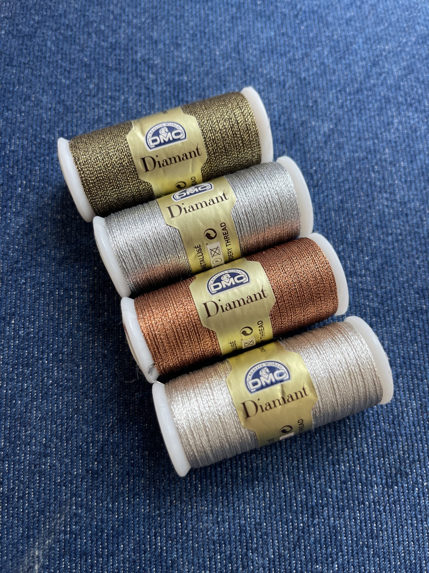 Carretéis de linha metálica DMC Diamant em várias cores sobre tecido azul