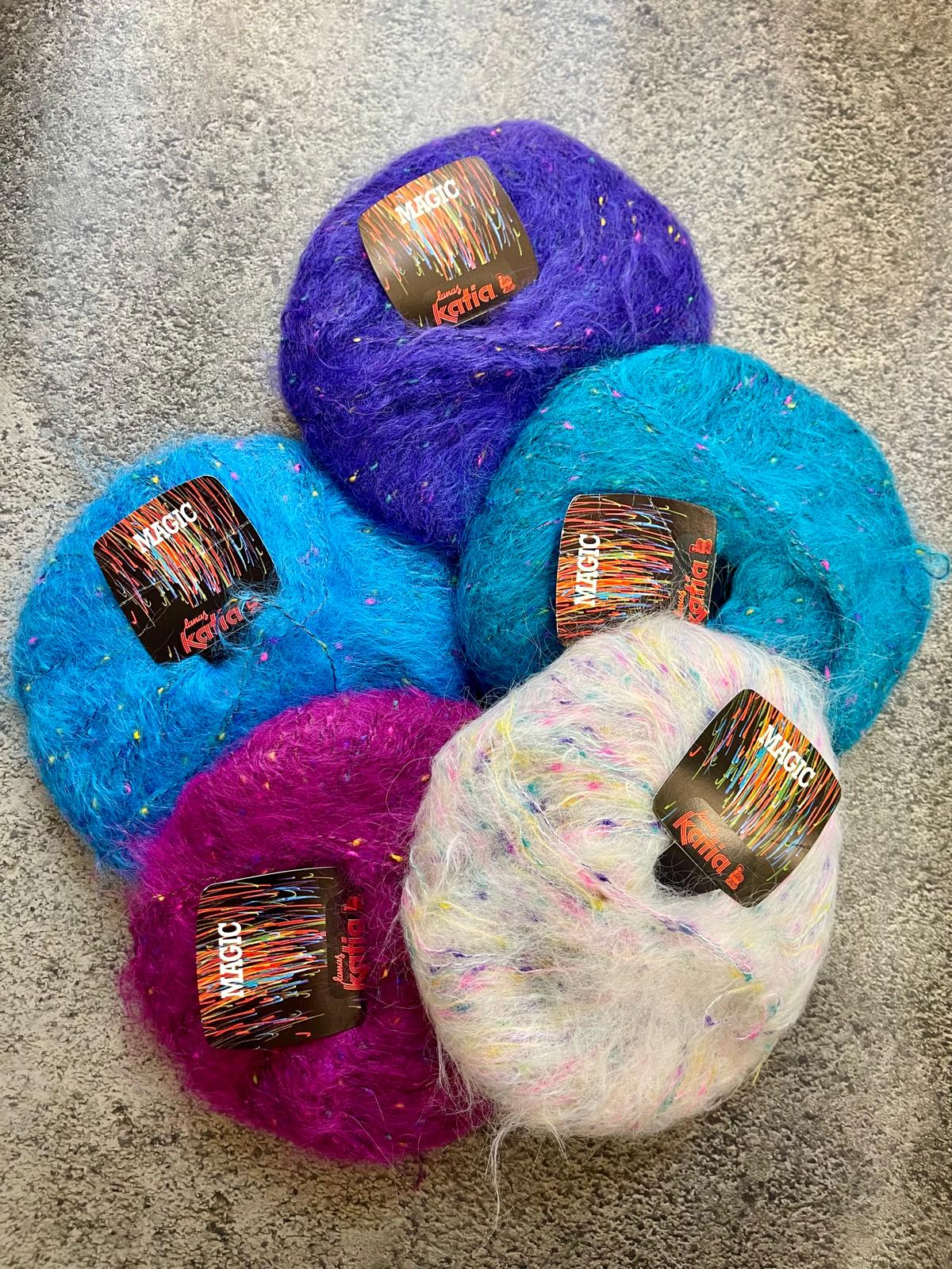 Cinco novelos de lã felpuda colorida com etiquetas e superfície cinzenta.