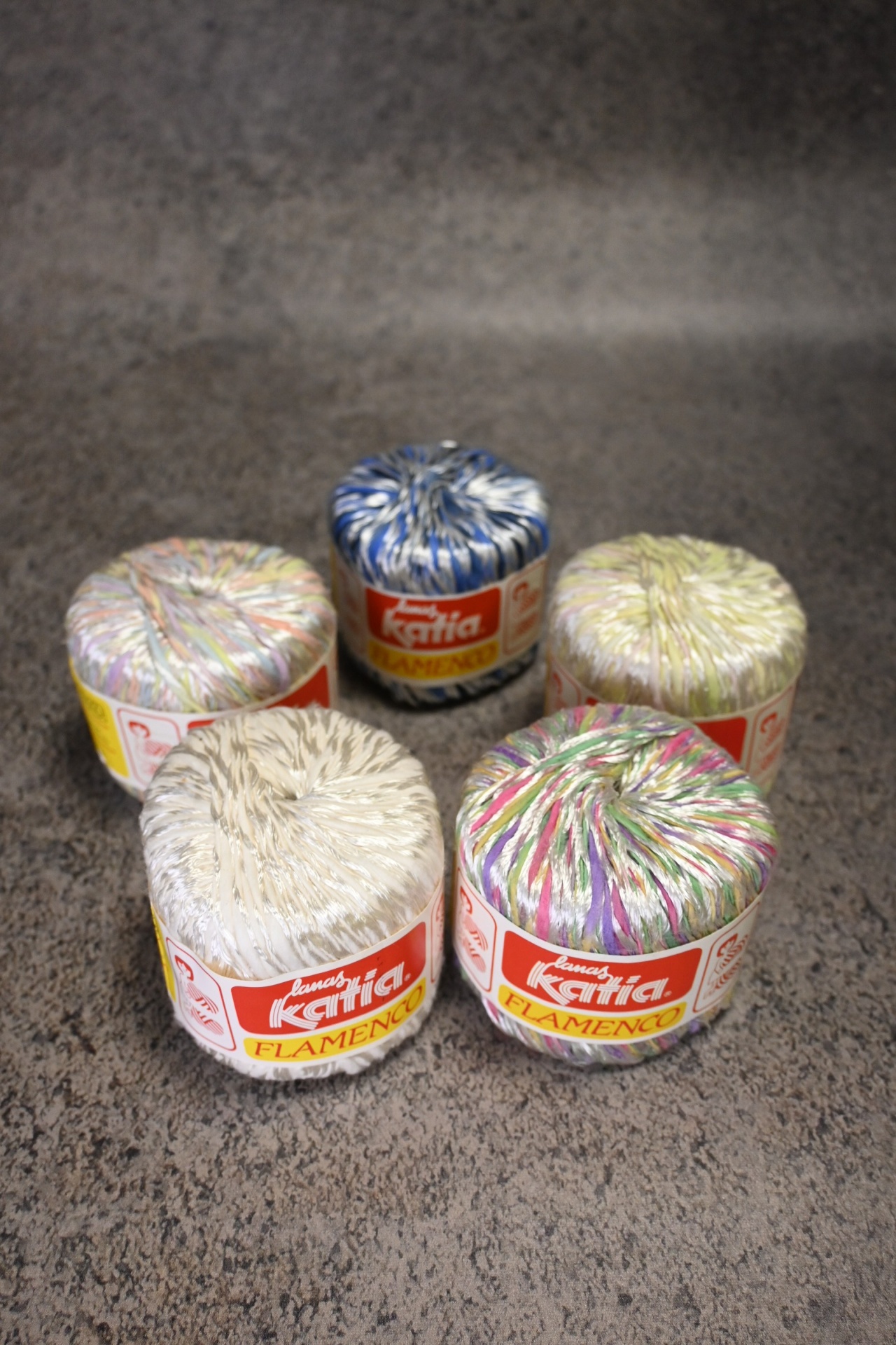 Novelos de fio Katia Flamenco coloridos em superfície cinzenta