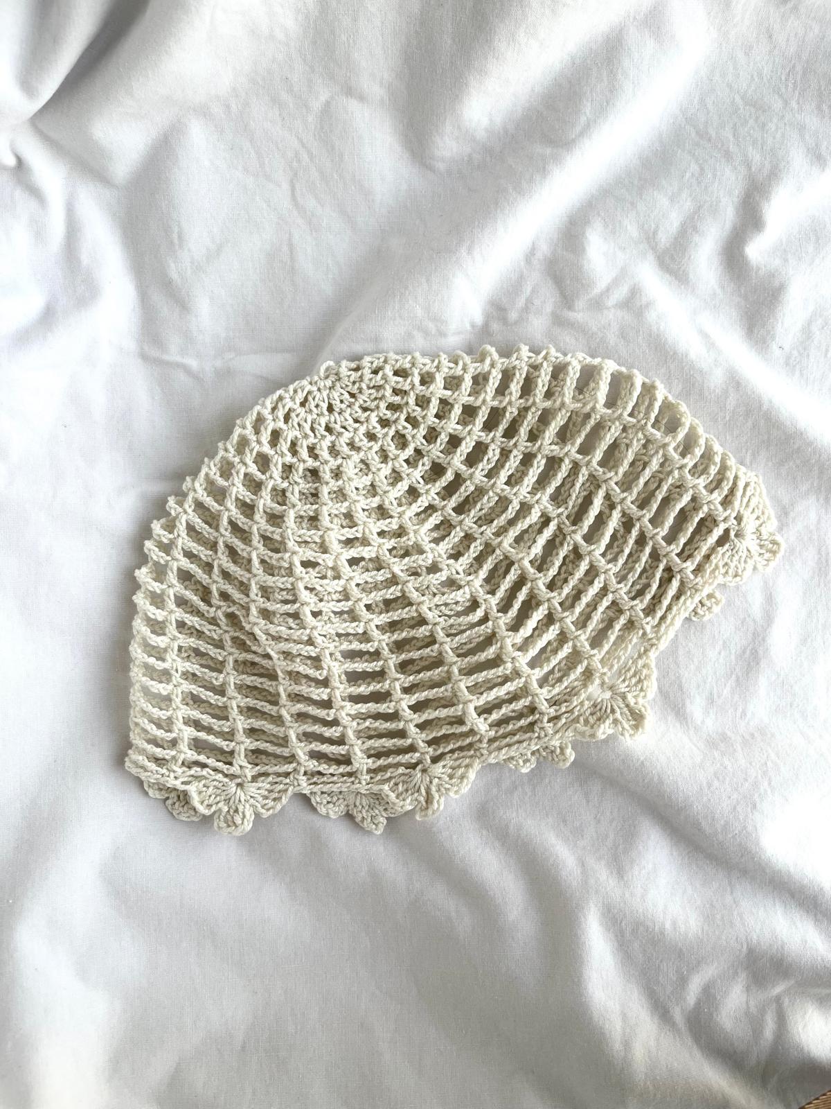 Boina de crochet bege clara com padrão de malha aberta em tecido branco