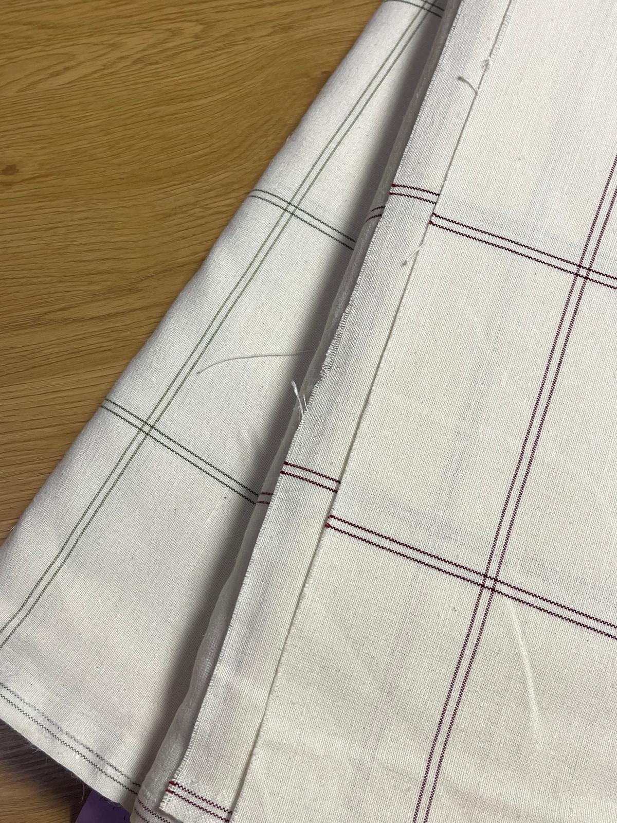 Tecidos brancos com padrão xadrez em vermelho e cinzento sobre madeira clara