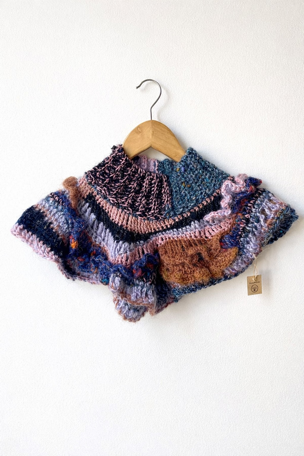 Capa tricô colorida pendurada num cabide de madeira