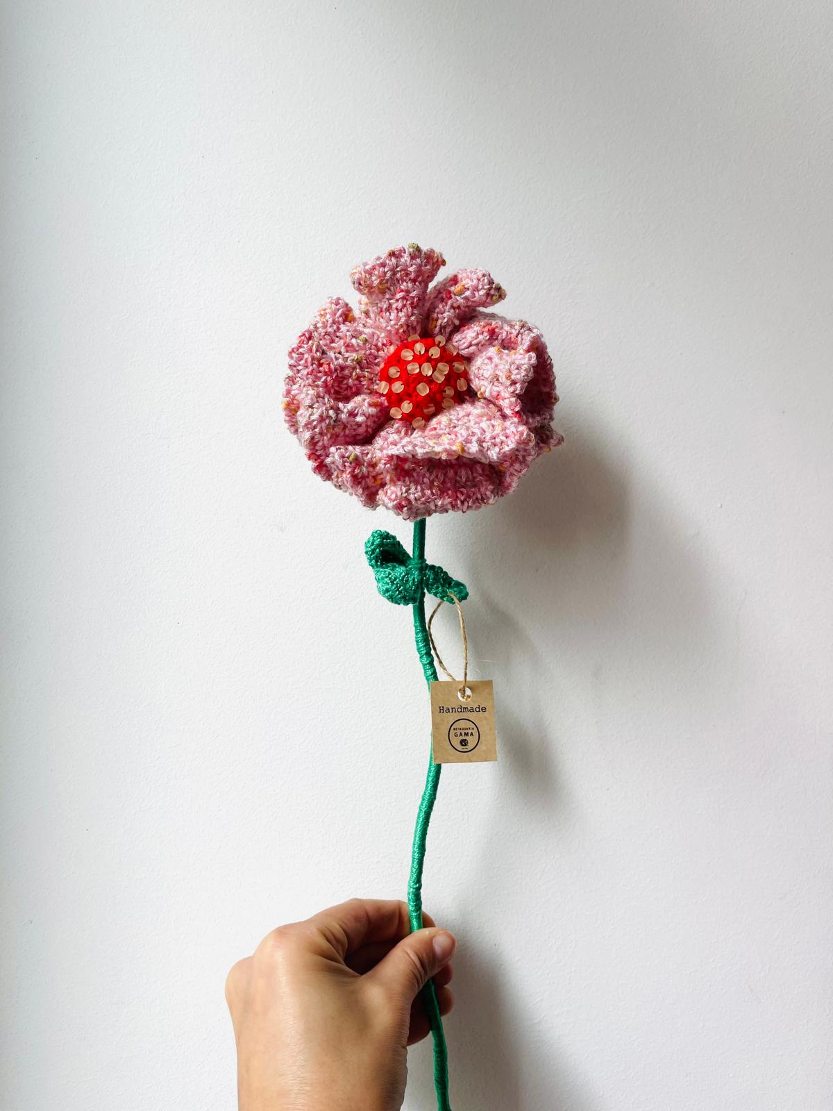 Flor artesanal de malha cor-de-rosa com centro vermelho e etiqueta Handmade