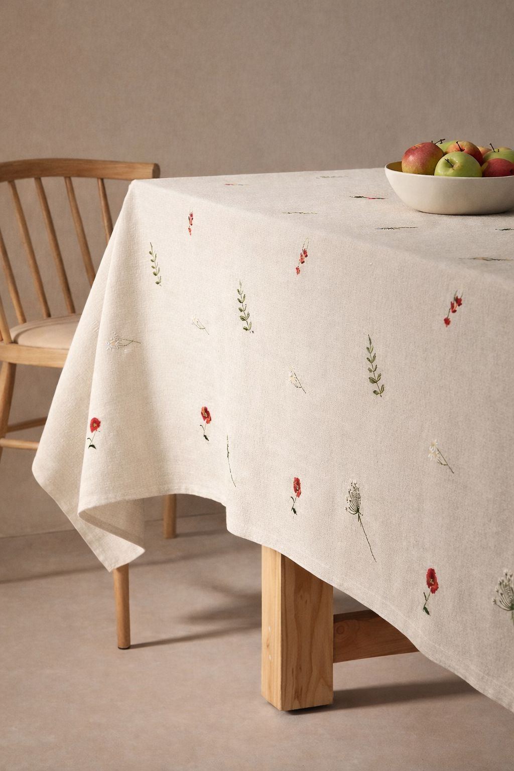 Toalha de mesa de linho bege claro com bordados florais e cesto com maçãs sobre mesa de madeira