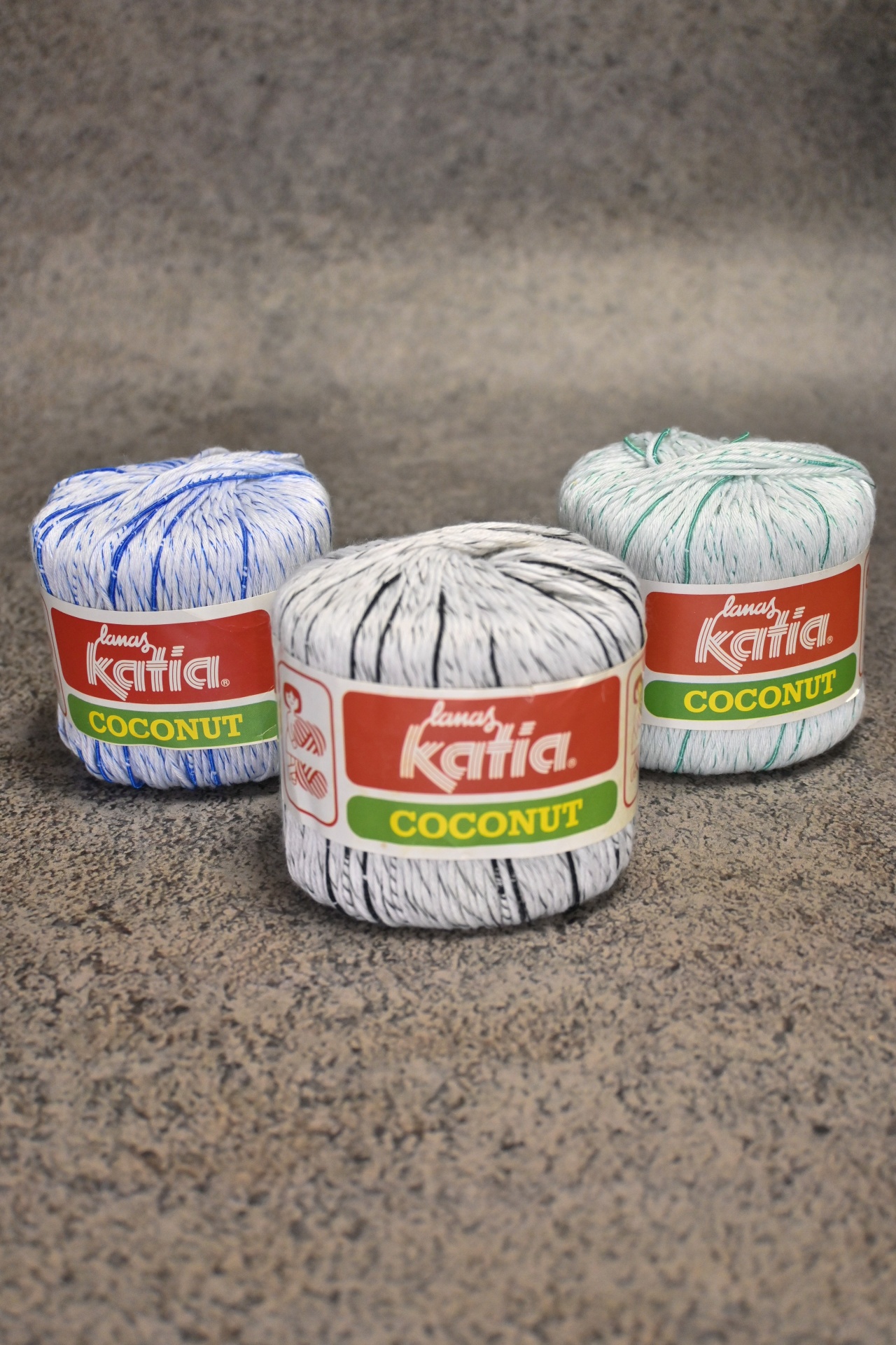 Três novelos de linha branca com riscas coloridas da marca Katia Coconut