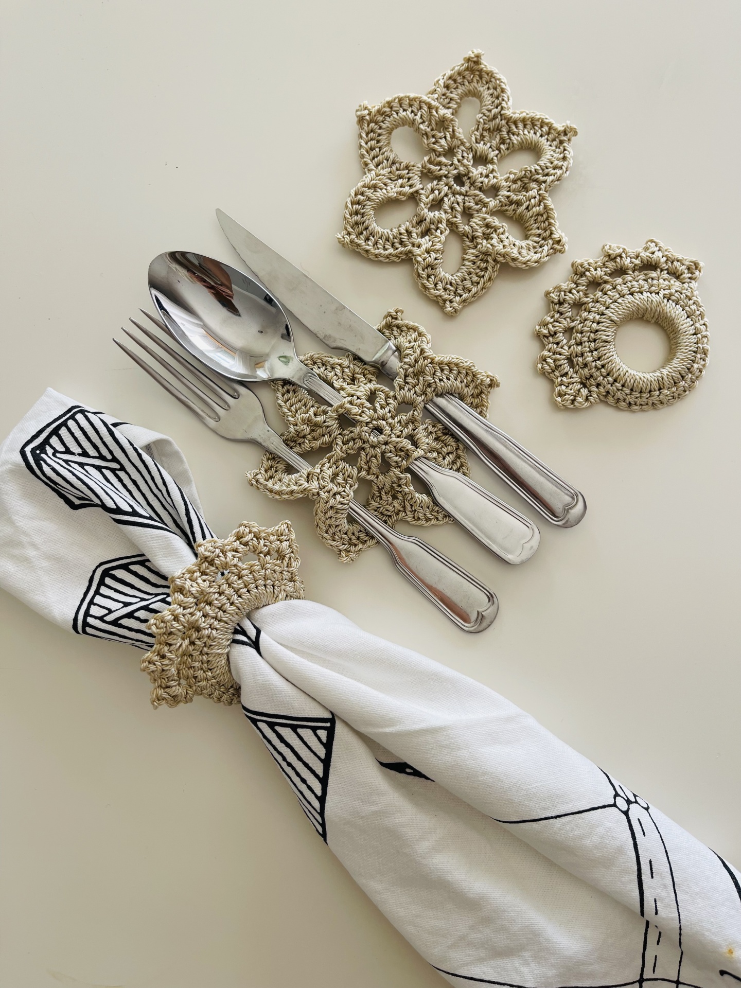 Argolas de guardanapo e porta-talheres em croché bege com talheres e guardanapo branco com padrão preto