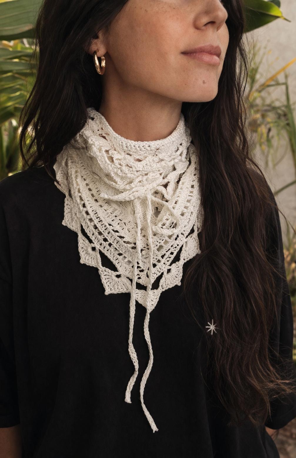 Lenço triangular branco em crochet com padrão rendado ao pescoço de mulher com t-shirt preta e bordado de estrela.