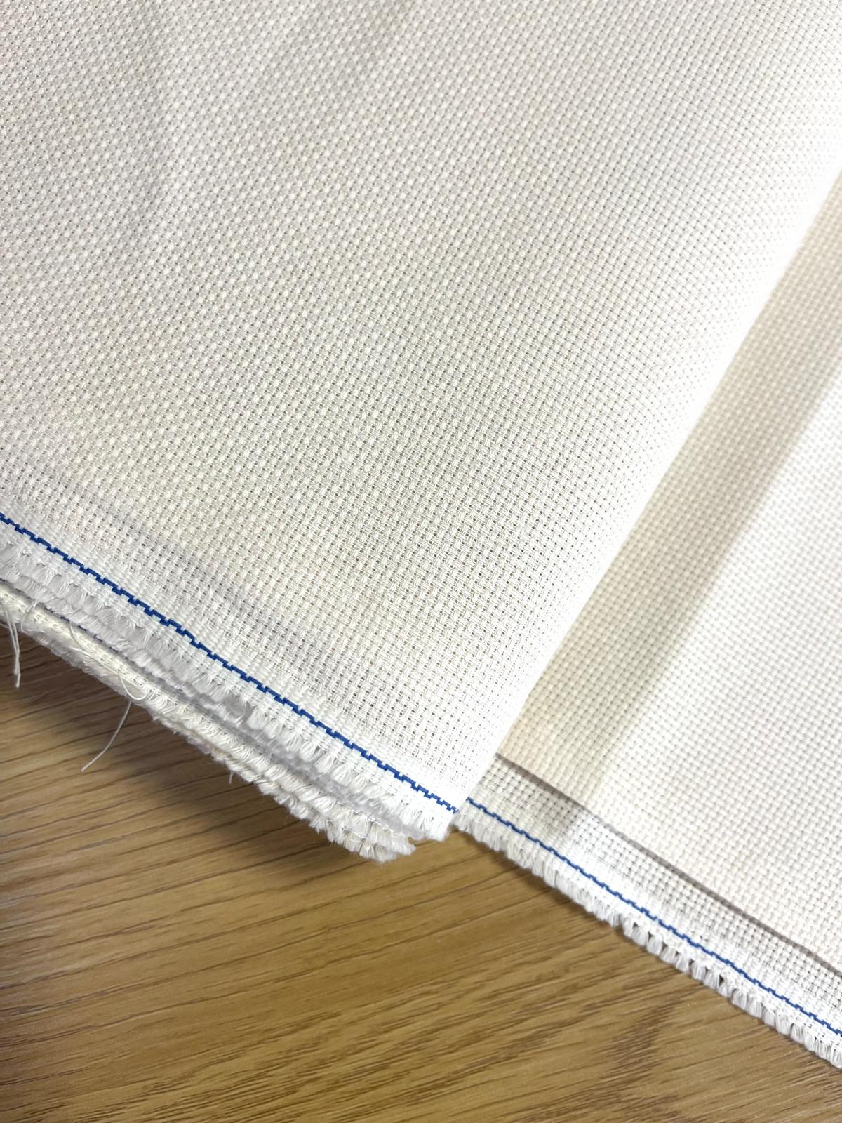 Tecido branco com textura quadriculada e costura azul sobre madeira clara