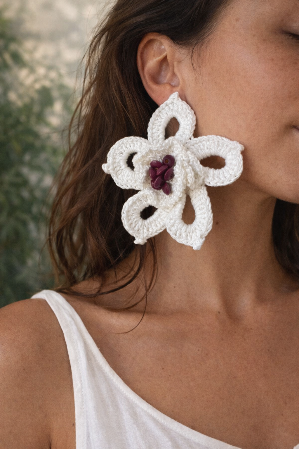Brinco grande de flor em crochet branco com contas roxas ao centro, usado por mulher