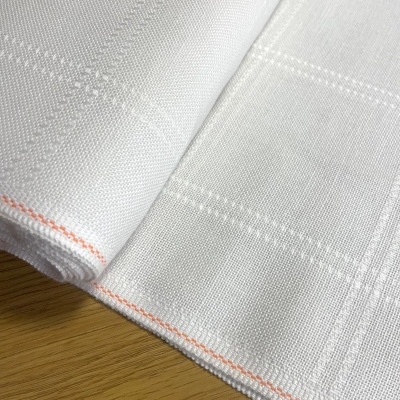 Pano branco com padrão quadriculado e borda laranja sobre mesa de madeira