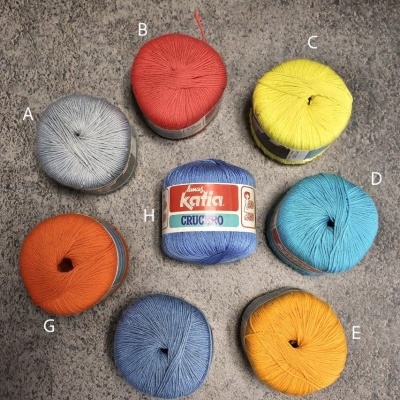 Oito novelos de linha coloridos etiquetados dispostos em círculo sobre superfície cinzenta.