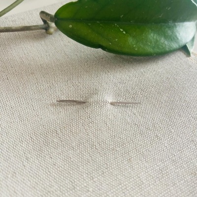 Agulhas de costura em metal sobre tecido branco com folhas verdes ao fundo