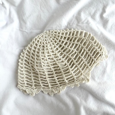 Boina de crochet bege clara com padrão de malha aberta em tecido branco