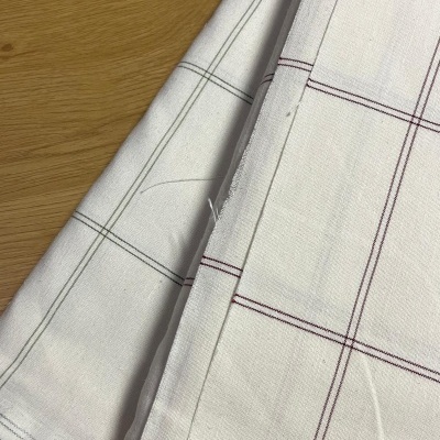 Tecidos brancos com padrão xadrez em vermelho e cinzento sobre madeira clara