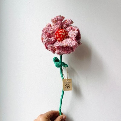Flor artesanal de malha cor-de-rosa com centro vermelho e etiqueta Handmade
