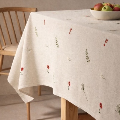 Toalha de mesa de linho bege claro com bordados florais e cesto com maçãs sobre mesa de madeira