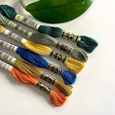Novel de linha para bordado coloridos com etiquetas DMC junto a folhas verdes.