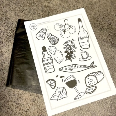 Papel ilustrado com desenhos em preto de alimentos e bebidas sobre superfície cinzenta e saco preto