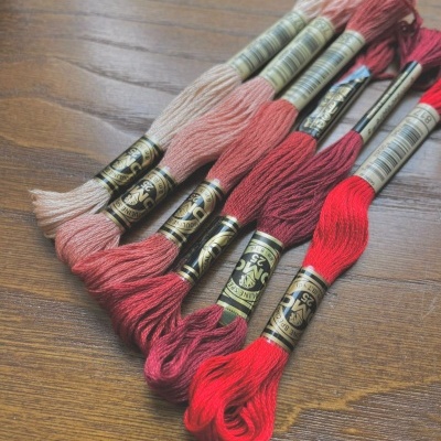 Sete madeixas de linha de bordar DMC em tons do bege ao vermelho sobre madeira