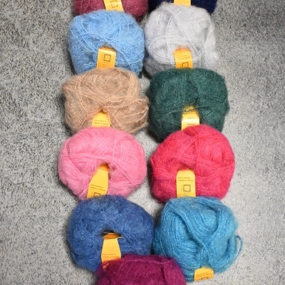 Dez novelos de lã colorida com etiquetas amarelas em fundo cinzento.