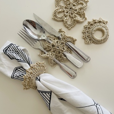Argolas de guardanapo e porta-talheres em croché bege com talheres e guardanapo branco com padrão preto