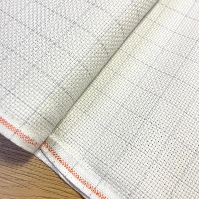 Tecido branco quadriculado com detalhes laranja numa superfície de madeira