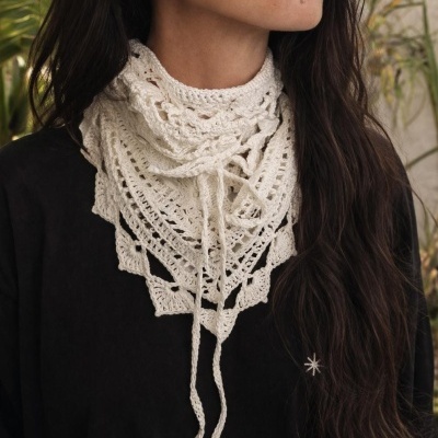 Lenço triangular branco em crochet com padrão rendado ao pescoço de mulher com t-shirt preta e bordado de estrela.