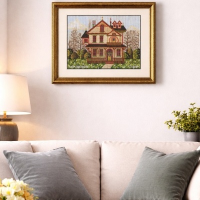 Tapeçaria de casa colorida numa moldura dourada pendurada numa parede branca acima de um sofá bege.